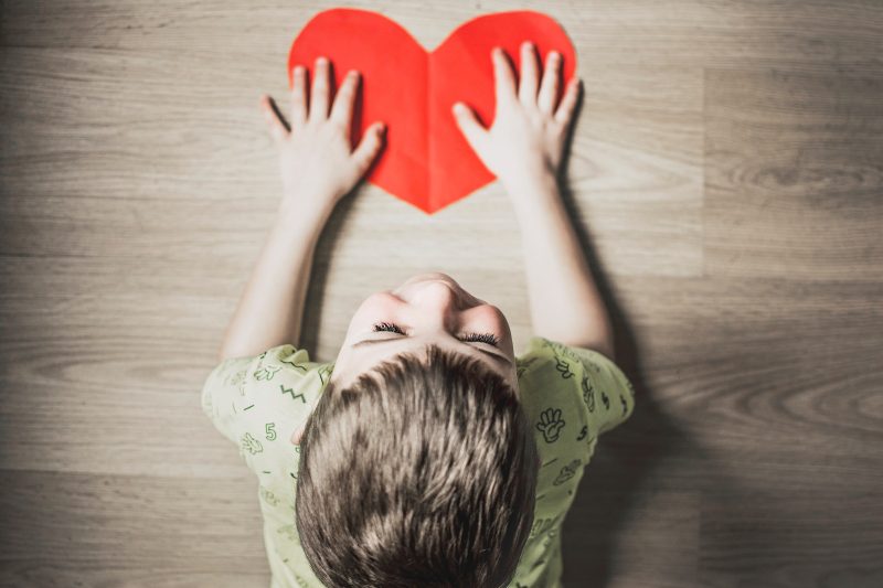 Ребенок держит ручки на красном сердечке